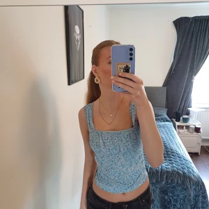 Blommig blå topp Gina Tricot - Supersöt blå topp från Gina Tricot i storlek S. Toppen har ett blommigt mönster i ljusblå och vita toner, breda axelband som man kan skustera till lite smalare och en fyrkantig urringning. Materialet är mjukt, perfekt sommaren. Där bak är det lite mer synligt om ni kan se de på bilden ❤️