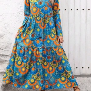 Färgstark långklänning med boho-mönster - Långklänning i boho-stil med färgstarkt mönster i blått, orange och gult. Klänningen har lång ärm, v-ringning och volangdetaljer. Luftig passform och tillverkad i mjukt material, perfekt för sommarens alla äventyr.