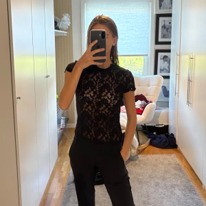 Svart spetsblus  - Säljer en svart, genombruten blus i spets med blommigt mönster. Modellen är kortärmad och har rund halsringning. 