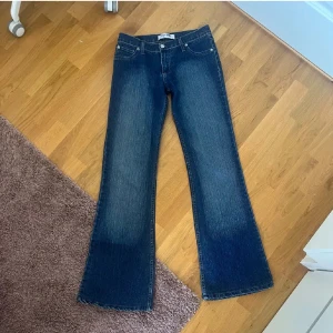 Tommy Hilfiger bootcut jeans blå - Snygga blå jeans från Tommy Hilfiger med bootcut passform. Klassisk femficksmodell med tydliga sömmar och Hilfiger-logga på bakfickan. Jeansen är i denim med lätt slitning och har normal midja. Perfekta för dig som gillar retrovibbar och bredare ben. de är i storlek M men små o storleken så passar absolut S