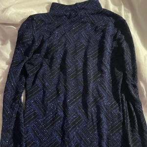 Glittrig marinblå kortklänning NLY One - Säljer en marinblå kortklänning från NLY One med glittrigt mönster och långa ärmar. Klänningen har ett snyggt geometriskt mönster i blått och svart som verkligen sticker ut. Perfekt för dig som vill ha något extra till kvällen!