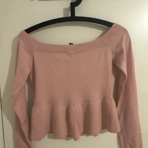 Rosa offshoulder topp med volang - Supersöt ljusrosa offshoulder topp med lång ärm och volang nertill. Mjuk och stretchig stickad känsla, perfekt för dig som gillar en feminin och trendig look. Passar snyggt till både jeans och kjol.