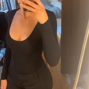 Svart långärmad topp med djup ringning - Säljer en svart långärmad body med djup, rundad urringning. Bodyn är tight och figurnära, lätt att styla