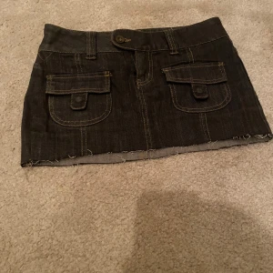 Svart jeansminikjol från Vero Moda - Mörkgrå jeansminikjol från Vero Moda med fickor både fram och bak. Skriv för mer info, pris går att diskutera.