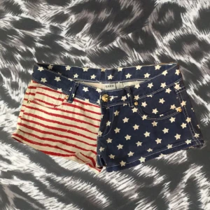Stjärn- och randmönstrade mini lågmidjade shorts  - Snygga shorts med amerikainspirerat mönster – ena sidan blå med vita stjärnor, andra sidan vit med röda ränder och små silvriga paljetter på bakfickan. Köpta på en vintage butik i Paris för 250kr. Klassisk jeansmodell med lågmidja och fickor med diamanter/rhinestones. Tveka inte på att kontakta mig vid frågor🩷