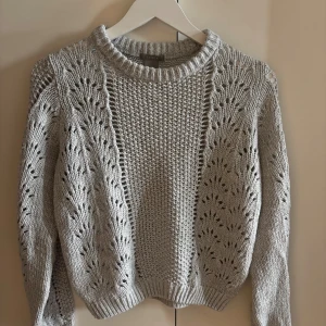 Grå stickad tröja från Lindex XS - Superfin grå stickad tröja från Lindex i storlek XS. Tröjan har ett snyggt hålmönster på ärmarna och sidorna samt ribbade muddar och krage. Perfekt för lager-på-lager och chill höst- och vinterstil.