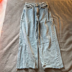Baggy ljusblå jeans från Never Denim - Baggy jeans från Never Denim i ljusblå tvätt med hög midja och råa, fransiga benslut. Jeansen har klassisk femficksdesign, breda ben och är tillverkade i bomullsdenim. Perfekta för en avslappnad och trendig look. Säljer pga används inte. Pris kan diskuteras. skriv för fler bilder. 