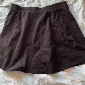 Svart kortkjol från Jacqueline de Yong - Enkel och stilren svart kortkjol från Jacqueline de Yong. Kjolen har en lätt utställd form och bred midjeresår för skön passform. Perfekt att matcha med en crop top eller stickad tröja. Materialet känns mjukt och följsamt.