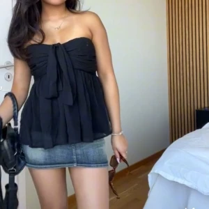 Vit omlott bandeau topp med knyt - Supersöt vit bandeau topp med omlott och knyt framtill. Tunt, flowy tyg med lätt rynkade detaljer och smala axelband som kan knytas runt halsen för halterneck-look. Det gör att knyta om runt halsen.