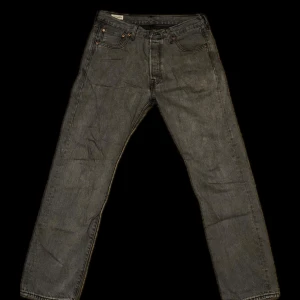 Levi's 501 grå jeans straight fit - Grå Levi's 501 jeans med klassisk rak passform och knappgylf. Jeansen har fem fickor, snyggt tvättad finish och ikonisk läderpatch bak i midjan. Perfekta för dig som gillar en tidlös look med streetkänsla.