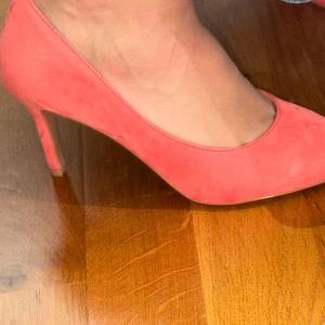 Korallrosa pumps från H&M - Snygga korallrosa pumps från H&M med spetsig tå och låg klack. Skorna är i mockaimitation och har en stilren design som ger en trendig look. Perfekta för dig som vill sticka ut med färg och stil.