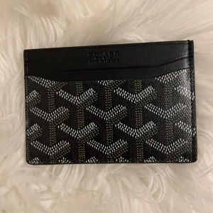 Svart Goy4rd plånbok med mönster - Snygg och stilren svart plånbok från Goy4rd med deras ikoniska grafiska mönster i vitt och grått. Plånboken är tunn och smidig, perfekt för kort och sedlar. Tillverkad i exklusivt skinn och levereras med originalask och kvitto.