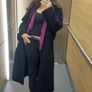 Massimo suttit kappa - Säljer en svart, lång och oversized kappa med klassisk krage och raka ärmar. Kappan har minimalistisk design och faller snyggt över kroppen. Perfekt för dig som gillar en clean och stilren look. DOCK saknar den bälte