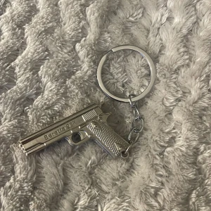 Beretta 92F Nyckelring - Snygg nyckelring i metall med en detaljerad miniatyr av Beretta 92F. Perfekt för samlare eller som present. Nyckelringen är i mycket gott skick utan synligt slitage eller repor. Ger ett exklusivt intryck och är både robust och stilren.
