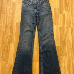 Blå bootcut jeans från Nelly - Snygga blå jeans från Nelly med bootcut-modell och klassisk femficksdesign. Jeansen har kontrastsömmar, dubbla knapphål i midjan och dekorativa bakfickor med vit broderad detalj. Perfekta för dig som gillar en retroinspirerad look.