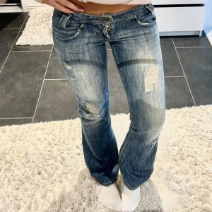 Blå bootcut jeans med slitningar - Snygga blå jeans med bootcut-modell och slitna detaljer framtill. Låg midja och klassisk femficksdesign. Jeansen har en ljus tvätt och är tillverkade i denim med lite stretch för skön passform. Midjemåttet är ca 34 cm och innerbenslängden 76 cm