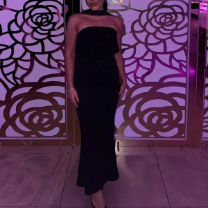 Svart axelbandslös långklänning - Säljer en elegant svart axelbandslös långklänning med figurnära passform. Klänningen har en stilren och tidlös design som ger en snygg siluett. Perfekt för dig som vill sticka ut med en klassisk look.