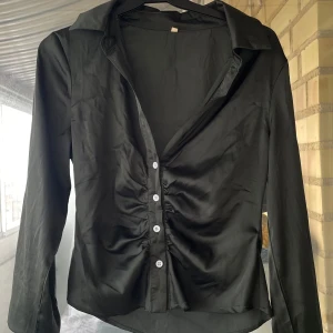 Grön  satinblus med rynk och knappar - Snygg grön blus i satinliknande material med lång ärm och klassisk krage. 