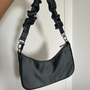 Grå axelväska  - Stilren grå axelväska med coolt scrunchie axelband och silvriga metalldetaljer.  Aldrig använd! 