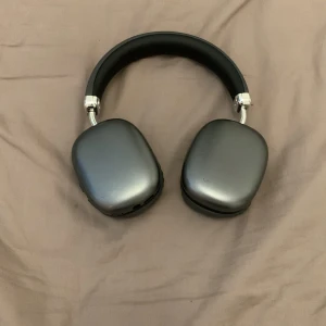 Trådlösa over-ear hörlurar - Bekväma trådlösa over-ear hörlurar i metallicgrått med mjuka öronkuddar och vadderad bygel. Utrustade med volymkontroll och mikrofonknapp på kåpan. Hörlurarna ser ut att vara i gott skick utan synligt slitage eller repor.