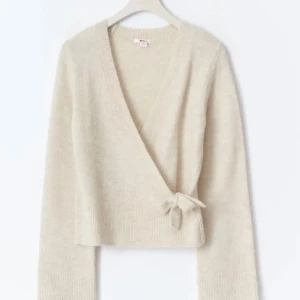 Beige omlottkofta med knyt - Supermysig beige omlottkofta med knyt i sidan och v-ringad hals. Koftan är stickad och har långa ärmar samt breda muddar. Perfekt för lager-på-lager och ger en chill men ändå stilren vibe. Storlek 