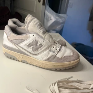 New Balance 550 sneakers vit/grå - Säljer ett par New Balance 550 sneakers i vitt och ljusgrått med klassisk retrodesign. Skorna har ovandel i skinn och mocka, meshpaneler och tydlig NB-logga på sidan. Platt sula och snörning, extra skosnören medföljer. Perfekta för dig som gillar stilrena och sportiga vibes. Nypris: 1400kr