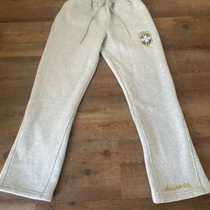 Brazil byxor - Snygga grå mjukisbyxor med broderad brasiliansk sköld på låret och chaiserão-logga vid benslutet. Byxorna har snörning i midjan och raka ben. Perfekta för chill eller sportiga dagar.