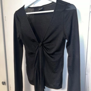 Svart långärmad topp med knyt - Svart långärmad topp med djup v-ringning och snygg knytning framtill. Från Gina Tricot, strl S.