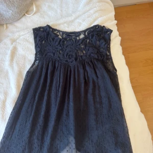 Svart spetsblus från KappAhl XS - Supersöt blus från KappAhl i storlek XS. Överdelen har ett detaljerat spetsmönster med blommor och mesh, medan nederdelen är lätt och luftig med små prickar.
