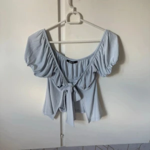 Ljusblå blus med puffärm från Gina Tricot - Supersöt ljusblå blus från Gina Tricot med puffiga korta ärmar och snygg knytning framtill. Toppen har en vid, rundad urringning och är tillverkad i mjuk bomull. Perfekt för dig som gillar romantiska och trendiga detaljer.