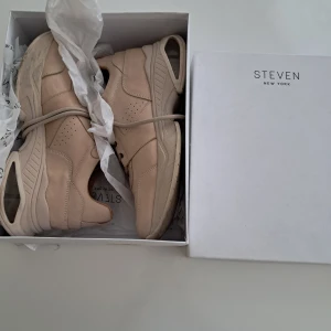 Beige sneakers från Steven New York - Chunky sneakers i läder med snygga paneler och perforerade detaljer. Skorna har platt sula med transparenta partier i hälen och rund tå. Klassisk snörning och mjuk insida för extra komfort. Perfekt för dig som gillar stilrena och trendiga sneakers. (Använda 1 gång)