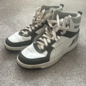 Snygga höga sneakers - Snygga high-top sneakers från Puma i vitt och grått med gröna detaljer. Skorna har snörning, rund tå och platt sula. Puma-logga på sidan och hälen.  Euro stl 41 (26,5cm)