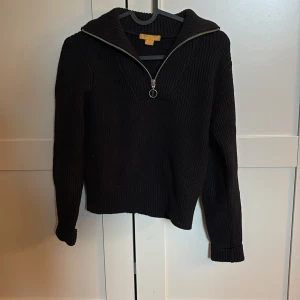 Svart stickad tröja med half zip - Svart stickad tröja med ribbad struktur och hög krage. Tröjan har en snygg half zip-dragkedja framtill och långa ärmar. Perfekt för lager-på-lager och chill höst- eller vinterstil.