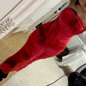 Röd axelbandslös långklänning - Säljer en snygg röd axelbandslös långklänning med coolt mönster i olika röda nyanser. Klänningen har en figurnära passform och är gjord i ett glansigt, mjukt material som ger en lyxig känsla. Perfekt för dig som vill sticka ut med en elegant och modern look. Aldrig använd 