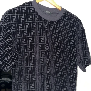 Svart sammetst-shirt från Fendi - Exklusiv svart t-shirt från Fendi i mjuk sammet med det ikoniska FF-mönstret över hela plagget. Klassisk rund halsringning och korta ärmar. Perfekt för dig som vill sticka ut med en lyxig och trendig look.