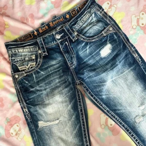Rock Revival blå jeans med broderi - Säljer ett par as feta blå jeans från Rock Revival med slitna detaljer och tydliga kontrastsömmar. Säljer då de var lite långa för mig. Jeansen har broderade bakfickor med unika mönster och en loose passform. Materialet är klassisk denim och färgen är tvättad blå med ljusa partier. Pris kan diskuteras!🤗🤗