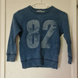 Blå sweatshirt med tryck 82 - Blå sweatshirt från Mywear med stort tryck av siffran 82 framtill. Tröjan har rund hals, ribbade muddar vid ärmslut och nederkant samt lång ärm. Perfekt för en avslappnad och sportig look. Det är någon fläck på framsidans nederkant men inget som stör helhetsintrycket. 