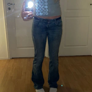 Blå bootcut jeans från H&M Divided - Snygga blå bootcut jeans från H&M Divided i storlek 34. Jeansen har klassisk femficksdesign, låg midja och utsvängda ben. Tillverkade i mjukt denim med snygga slitningar och detaljerade bakfickor med lock. Jag har använt de ganska mycket men de är fortfarande i bra skick. De är bra längd för mig som är 165cm. Jag brukar ha midja 24-26 och dehär passar perfekt i midjan. Jag säljer de för att jag inte använder de lika mycket nu när jag har fler par jeans. 