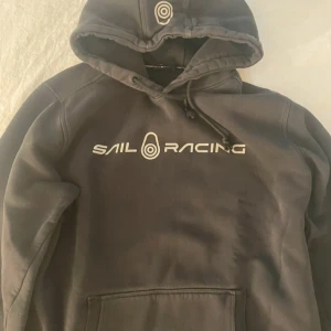 Svart  Sail Racing hoodie med tryck  - Len och fluffig inuti så ej urtvättad. Svart sailracing hoodie i storlek L passar bättre M. Inga defekter eller liknande. Hör av dig om du undrar något 🙏🤍🩷
