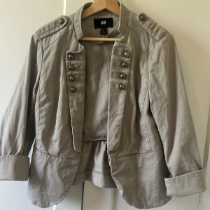 Grå kappa tre kvarts ärmad - Snygg gå kappa från H&M. Med knappar och tre kvarts ärmar och markerad midja med lätt volang baktill. Perfekt till hösten! 🩶