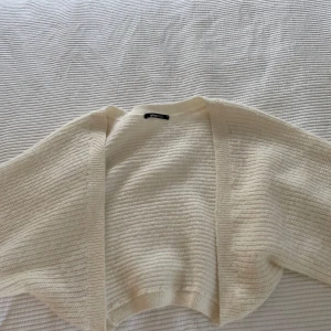 Krämvit stickad kofta från Gina Tricot - Mysig krämvit stickad kofta från Gina Tricot i storlek XS. Koftan är öppen framtill, har lång ärm och är ribbstickad för en chill och avslappnad vibe. Perfekt att slänga över en topp när det är lite kyligt ute. Bolero kofta!