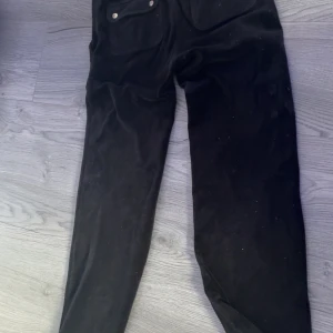 Svarta mjukisbyxor Juicy Couture XXS - Svarta mjukisbyxor från Juicy Couture i supermjuk velour. Byxorna har raka ben, bred resår i midjan och stora fickor framtill. Perfekta för en chill och trendig look. Klassisk Juicy-stil som aldrig går ur tiden.