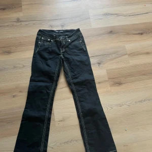 Svarta bootcut byxor med broderi - Svarta byxor med kontrasterande vita sömmar och bootcut-modell. Snygga broderade detaljer på bakfickorna med knappstängning. Klassisk femficksdesign och låg midja. Perfekta för dig som vill sticka ut med coola detaljer.