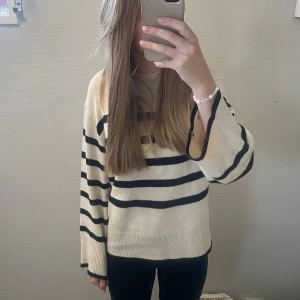 Randig stickad tröja i beige och svart - Säljer en snygg stickad tröja med breda svarta ränder på beige botten. Tröjan har en relaxed passform, rund hals och långa ärmar. Perfekt för dig som gillar en klassisk men trendig look.