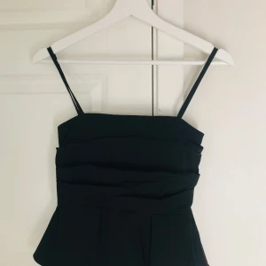 Svart fin topp med smala axelband - Säljer en svart fin topp med smala justerbara axelband och snygga veckade detaljer framtill. Klänningen har en figurnära överdel och lätt utsväng ner! Säljer en likadan i vit ☺️