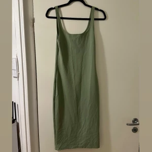 Grön ärmlös långklänning - Enkel och stilren grön långklänning med raka linjer och breda axelband. Klänningen är ärmlös och har en mjuk, bekväm känsla som passar perfekt till varma dagar. Snygg att styla med sneakers eller sandaler.