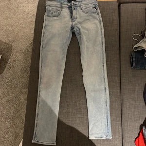 Replay Anbass ljusblå jeans, stl 30 - Säljer ett par Replay Anbass jeans i ljusblå tvätt med klassisk femficksdesign och snygga detaljer på bakfickorna. Jeansen har smal passform och är tillverkade i mjukt denimtyg som sitter riktigt bra. Perfekta för dig som gillar stilrena och moderna jeans längd 32.