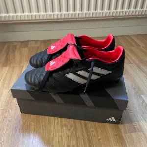 Adidas Copa Gloro FG fotbollsskor svart/röd - Säljer ett par Adidas Copa Gloro FG fotbollsskor i svart med röda detaljer och silvriga ränder. Klassisk design med snörning och täckande plös. Perfekta för spel på gräsplan. Snygg kontrast mellan svart och rött, samt bekväm passform. Endast använd ett fåtal gånger på fotbollsplanen ⭐️ storlek 42 🔥🔥