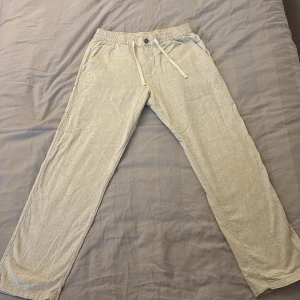 Beiga linnebyxor från H&M med snörning - Säljer ett par beiga linnebyxor från H&M i regular fit. Byxorna har elastisk midja med snörning och knapp, dragkedja samt sidofickor och en bakficka. Perfekta för chill dagar och sommarhäng. Använda enstaka gånger!