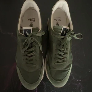 Olivgröna sneakers från Polo Ralph Lauren - Snygga gröna sneakers från Polo Ralph Lauren med klassisk logga på sidan. Skorna har snörning, ovandel i textil och mockadetaljer samt vit sula. Perfekta för dig som vill ha en stilren och sportig look.